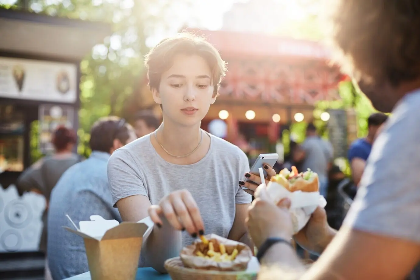 A couple is eating fries and a burger at a fair in a park on a sunny summer day and having a great time.